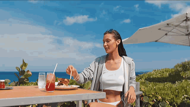 a woman in a bikini sits at a table eating a meal