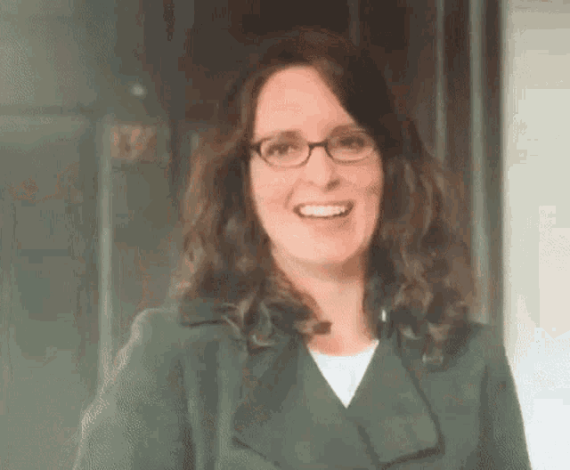 a woman wearing glasses and a green trench coat is smiling .