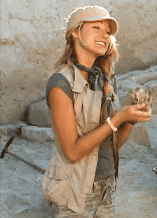 a woman wearing a hat and vest holds a rock in her hand