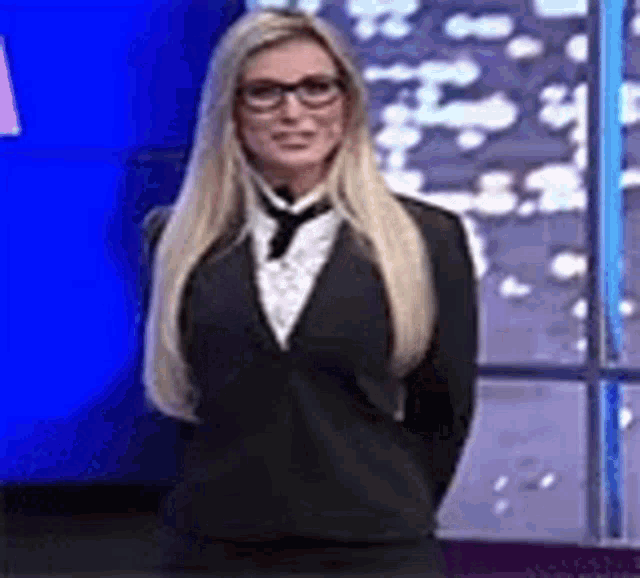 a woman wearing glasses and a suit is standing in front of a blue wall .