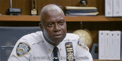 a man in a police uniform is sitting at a desk and says look at that you 've helped me find my smile .