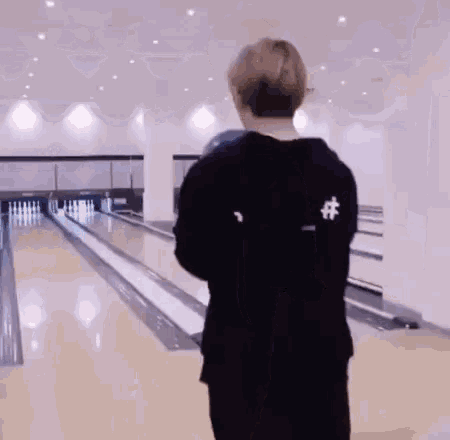 a man is playing bowling in a bowling alley while another man watches .