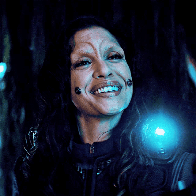 a woman with piercings on her face is smiling with a blue light behind her