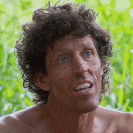 a shirtless man with curly hair and blue eyes is smiling and looking at the camera .