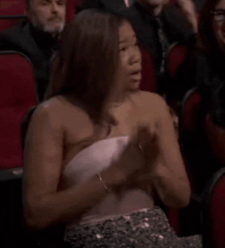 a woman in a pink dress is crying while sitting in a crowd of people .