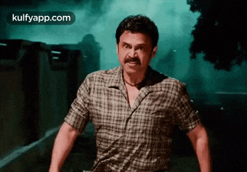 a man in a plaid shirt with a mustache is standing in front of a building .
