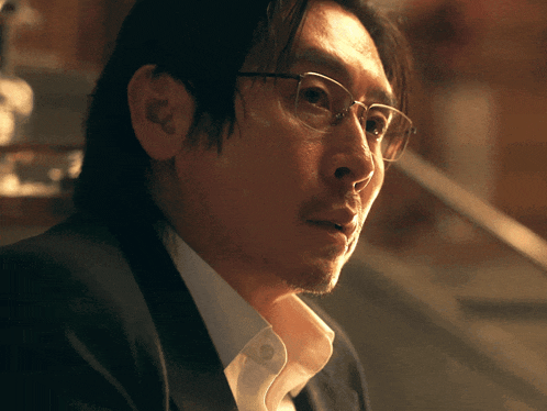 a man wearing glasses and a suit looks to his left