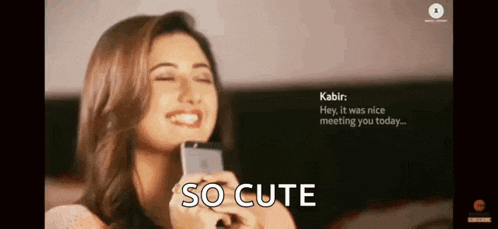 a woman is smiling while holding a cell phone and the words so cute are on the screen .