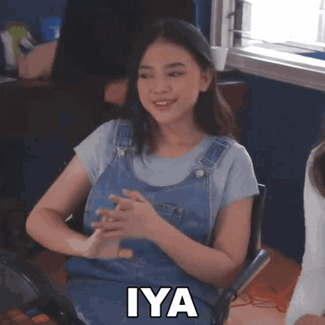 a girl in overalls is sitting in a chair with the word iya written on the bottom
