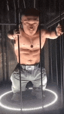 a shirtless man is standing in a cage with a light circle around him