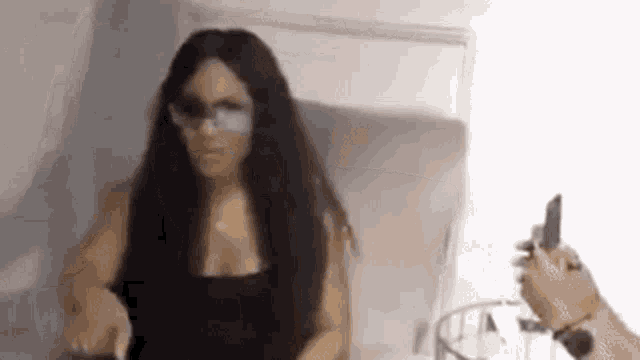 a woman wearing sunglasses is sitting on a bed while a man holds a cell phone .