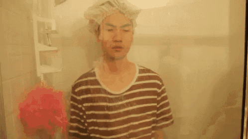 a man with a shower cap on his head is standing in a shower .