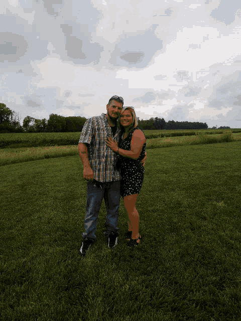a man and a woman pose for a picture in a field
