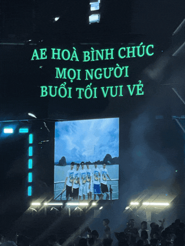 a group of people are standing in front of a screen that says ae hoa bình chuc