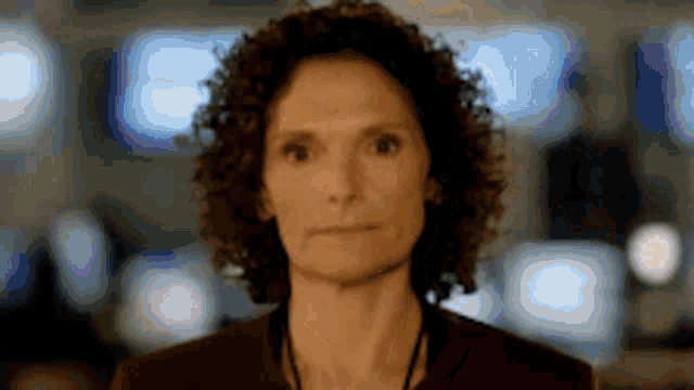 a woman with curly hair is looking at the camera with a serious expression on her face .