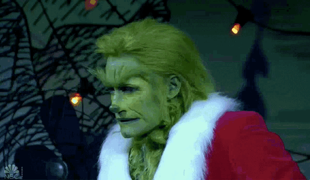 a woman dressed as the grinch is standing in front of a nbc sign
