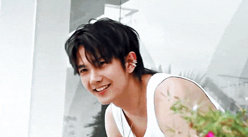 a young man wearing a white tank top is smiling and looking at the camera .