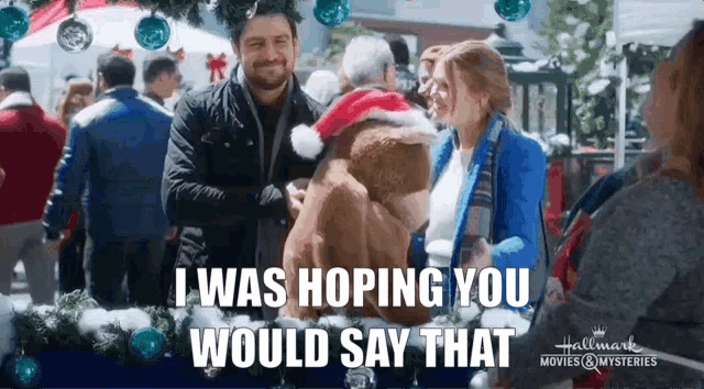 a man and a woman are holding a teddy bear at a christmas market . the man is wearing a santa hat .