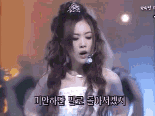 a woman in a white dress is singing into a microphone while wearing a tiara on her head .