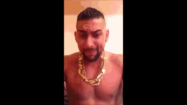 a shirtless man wearing a gold chain around his neck is looking down .