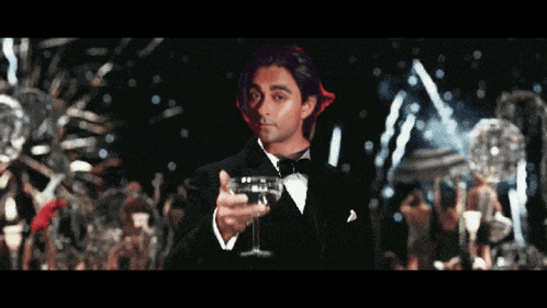 a man in a tuxedo holds a glass of wine
