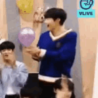 a man in a blue sweater is holding a balloon in front of a sign that says vlive