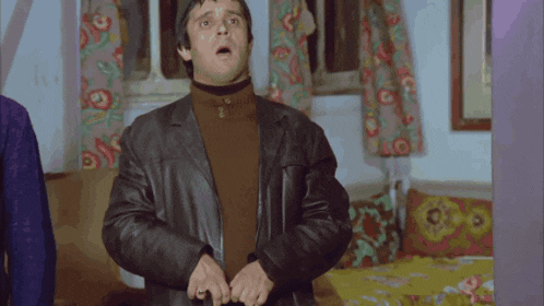 a man in a leather jacket is standing in a bedroom