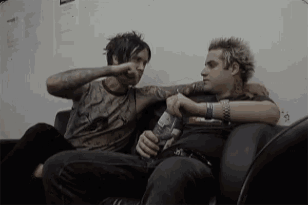 two men are sitting on a couch and one is holding a bottle of blue claw energy drink