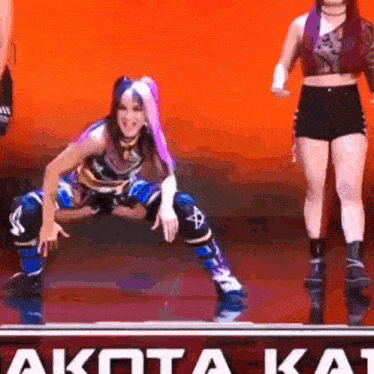 two women are dancing on a stage in front of a sign that says akota kat .