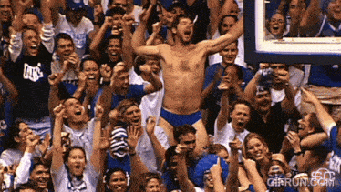 a shirtless man stands in front of a crowd wearing duke t-shirts