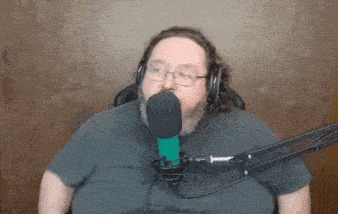 a man with glasses and a beard is speaking into a microphone .