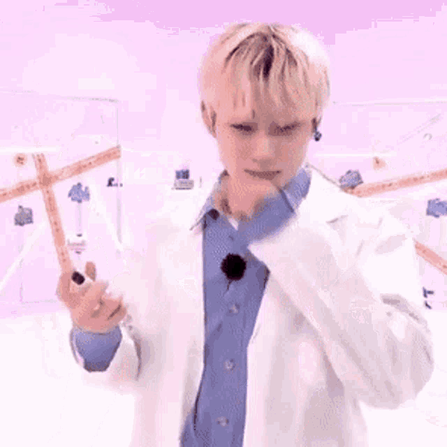 a young man wearing a white lab coat and a blue shirt is standing in front of a purple wall .
