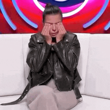 a woman in a leather jacket is sitting on a couch covering her face with her hands .