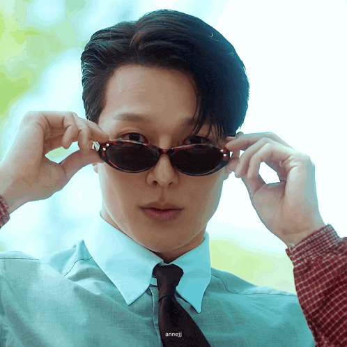 a man wearing sunglasses and a plaid shirt has the name anneji on the bottom of his shirt