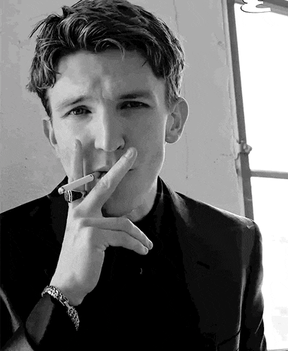 a man in a suit is smoking a cigarette in front of a window .