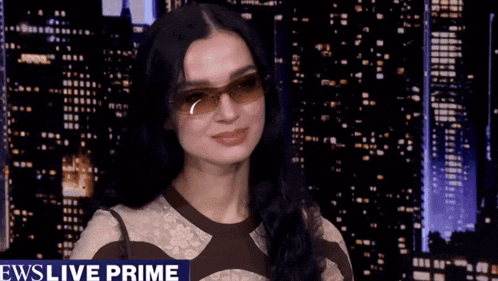 a woman wearing sunglasses is smiling in front of a news live prime banner
