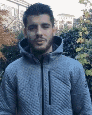 a man wearing a grey adidas jacket stands in front of trees