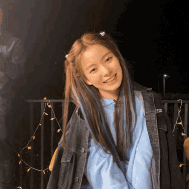 a girl wearing a blue hoodie and a denim jacket smiles