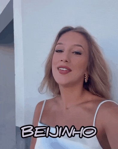 a woman in a white tank top is standing next to a sign that says beijinho on it