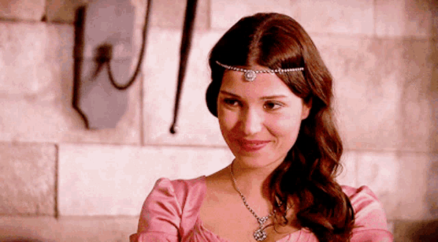 a woman wearing a pink dress and a headband smiles for the camera