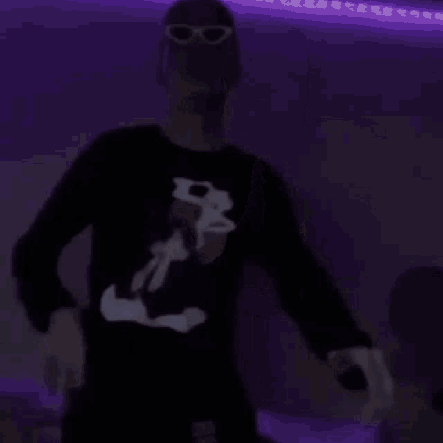 a man in a black shirt is dancing in a dark room with purple lights .