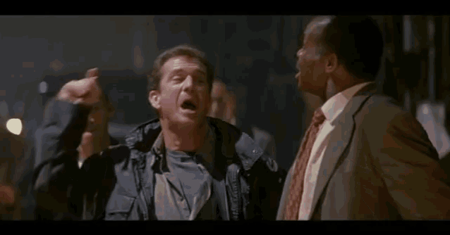 two men are standing next to each other in a dark room and one of them is pointing at the other .