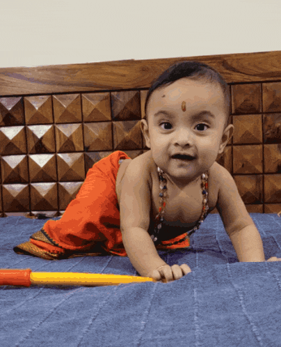 a baby crawling on a bed with a yellow stick in front of him