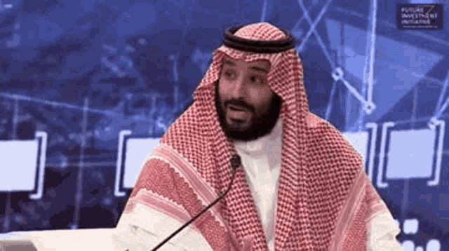 a man in a keffiyeh is sitting at a table with a microphone in front of him .
