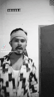 a man wearing a headband and a plaid shirt is standing in front of a door