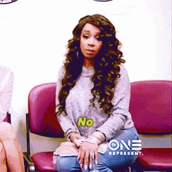 a woman with curly hair is sitting in a chair with the word no on her shirt