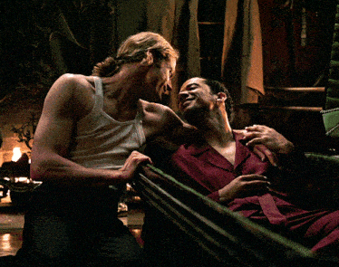 a man in a white tank top sits next to another man