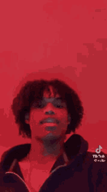 a young man with curly hair is smiling in front of a red wall .