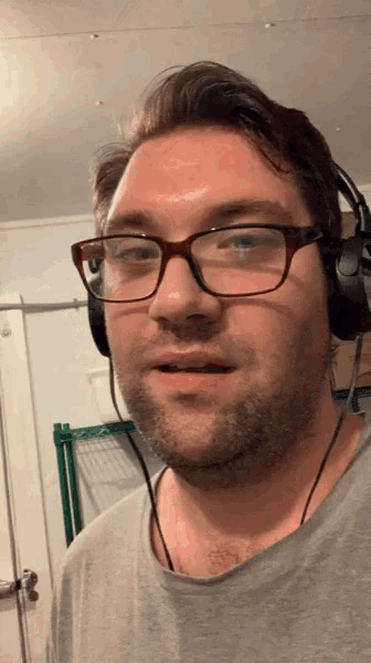 a man wearing glasses and headphones looks at the camera with a surprised look on his face