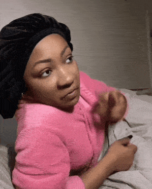 a woman wearing a pink sweater and a black hat laying on a bed